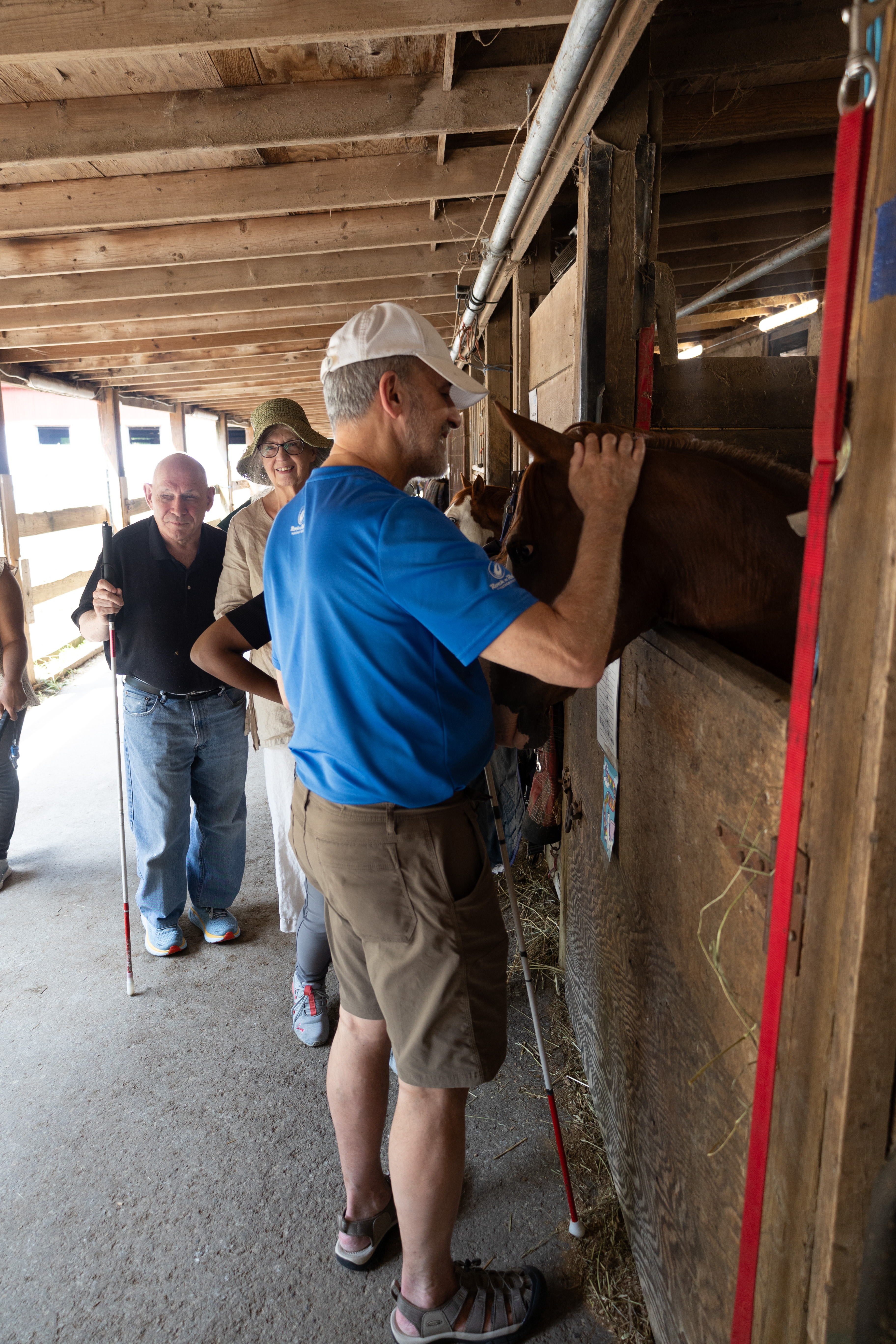 Photo of Testing Audio Description: Doug Powell and other ACB members in the horse barn (2024)